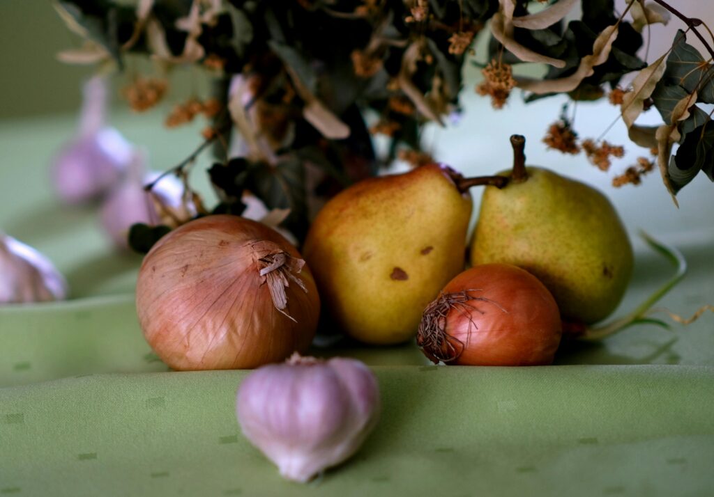 Artistic still life of pears, onions, garlic, and leaves on a green tablecloth.